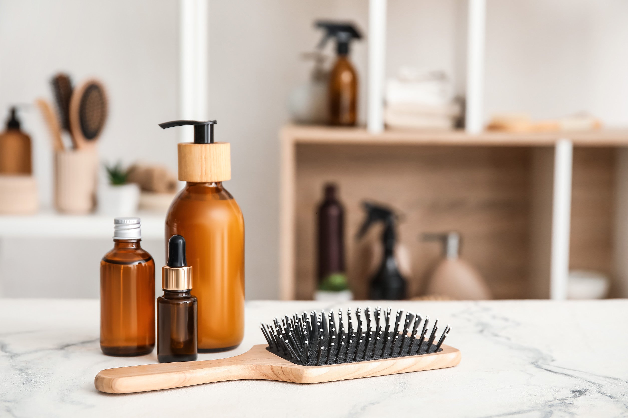 Natural hair care cosmetic products in glass bottles with comb on marble counter.