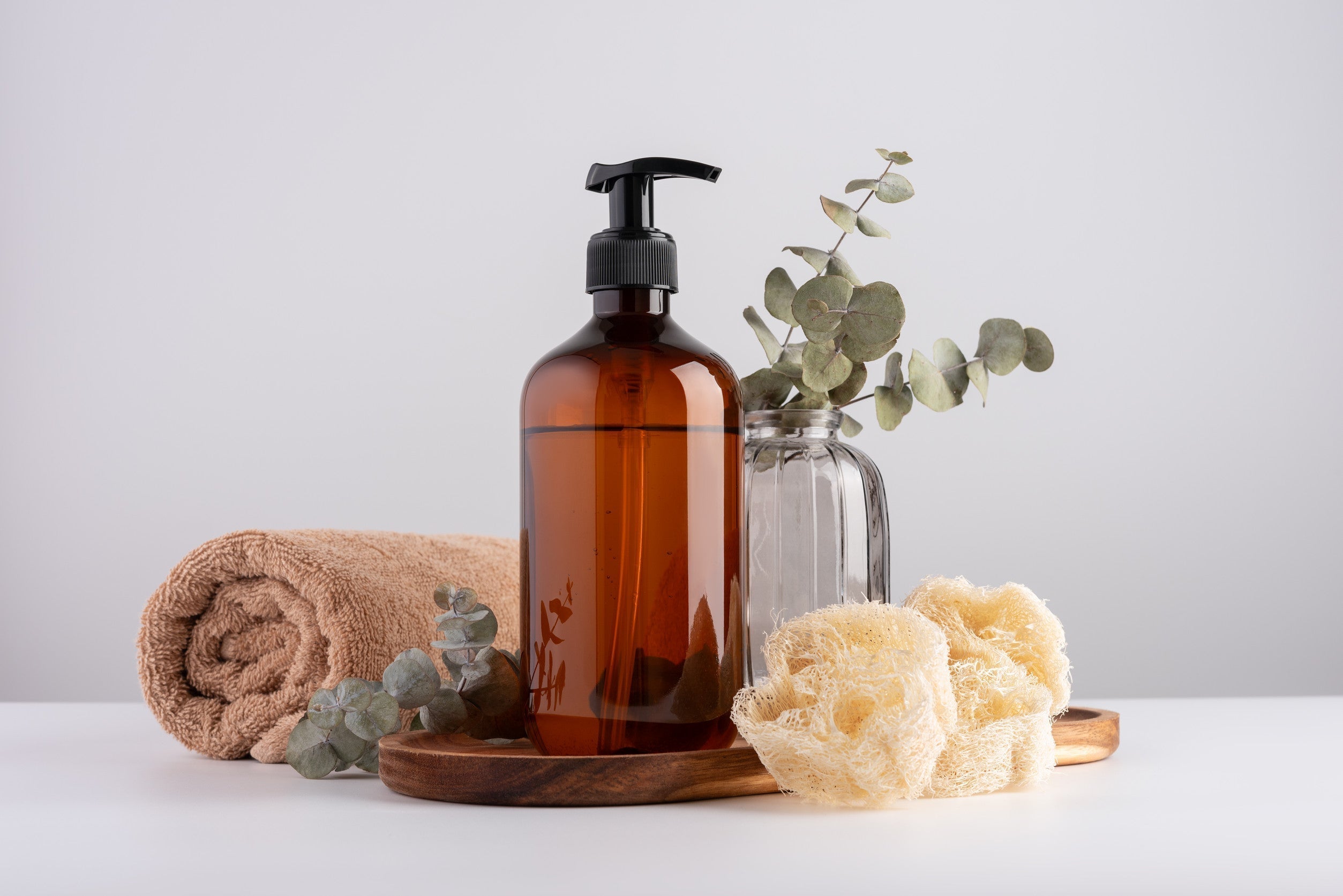 Bath and wellness still life with cotton towel and cosmetic bottle for healthy wellbeing. Brown transparent dispenser bottle, cotton towel, eucalyptus and sponges.