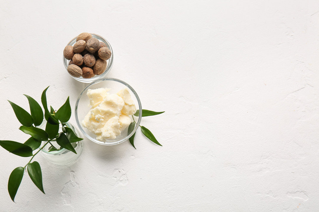 Bowls with shea butter and nuts on light background