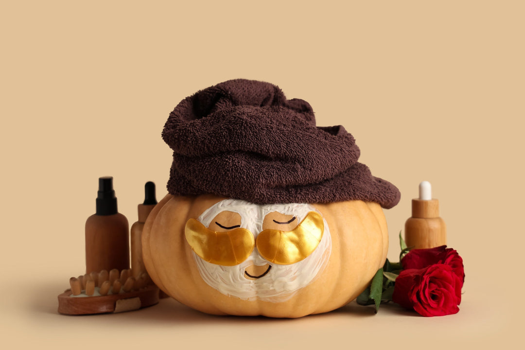 Pumpkin with under-eye patches, towel, cosmetics and rose flower on color background