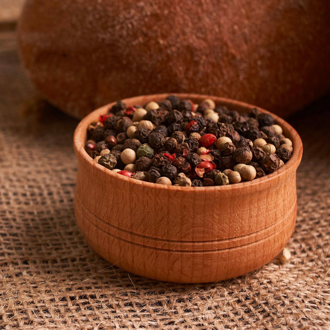 Wooden bowl filled with multicolored peppercorns on a rustic fabric background