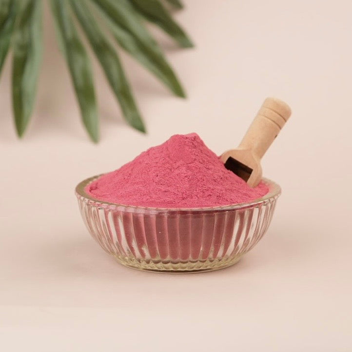 Pink powder in a glass bowl with a scoop and tan background
