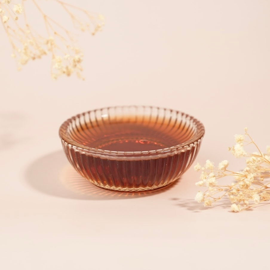 Glass bowl with a textured rim on a light beige background with dried flowers.
