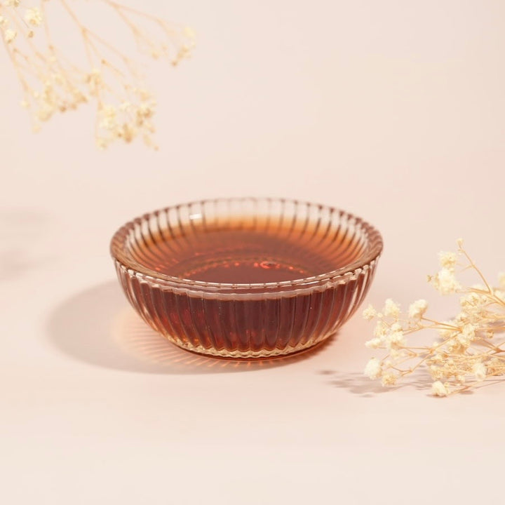 Glass bowl with a textured rim on a light beige background with dried flowers.