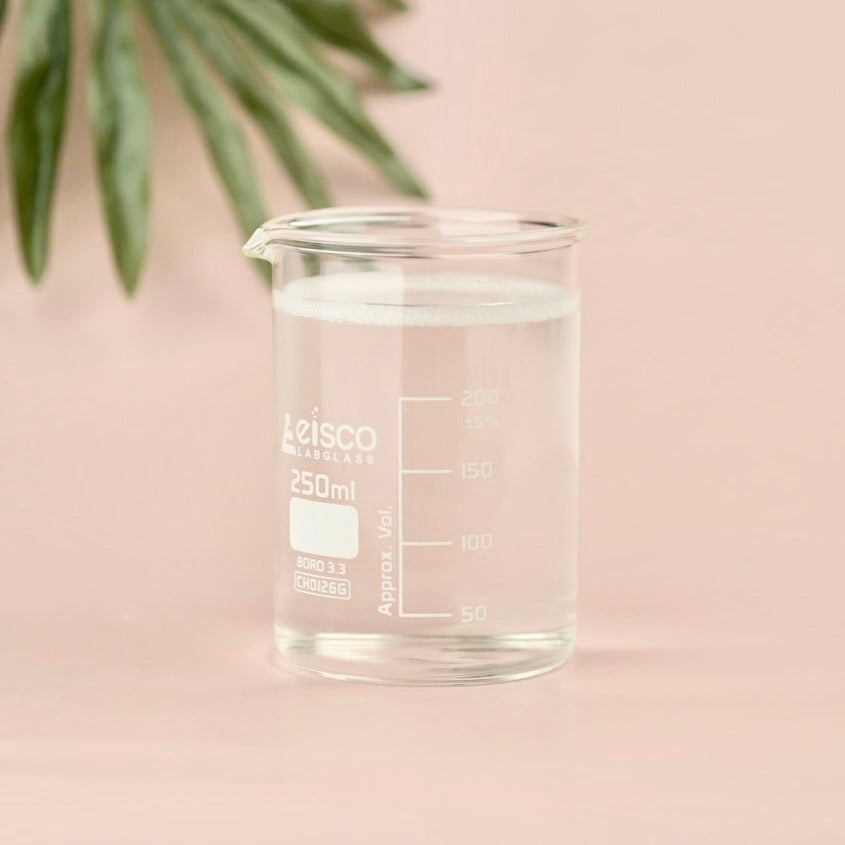 Clear beaker with measurement markings on a light pink background