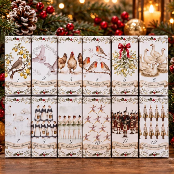 Twelve illustrated gift boxes arranged in a 3-by-4 grid on a wooden surface, decorated with Christmas-themed artwork such as birds, swans, a robin, mistletoe, and figures in historical dress. Festive greenery, red berries, and warm lights appear in the background.
