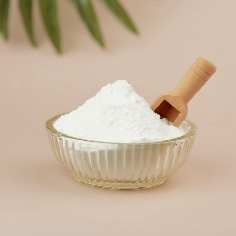 Glass bowl filled with white powder and a wooden scoop on a beige background