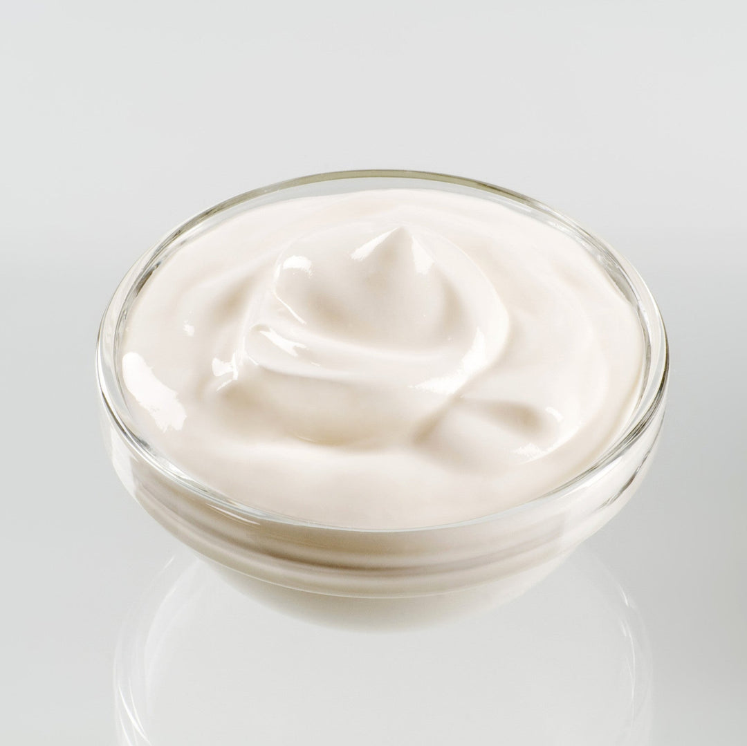 Glass bowl filled with white cream on a light gray background