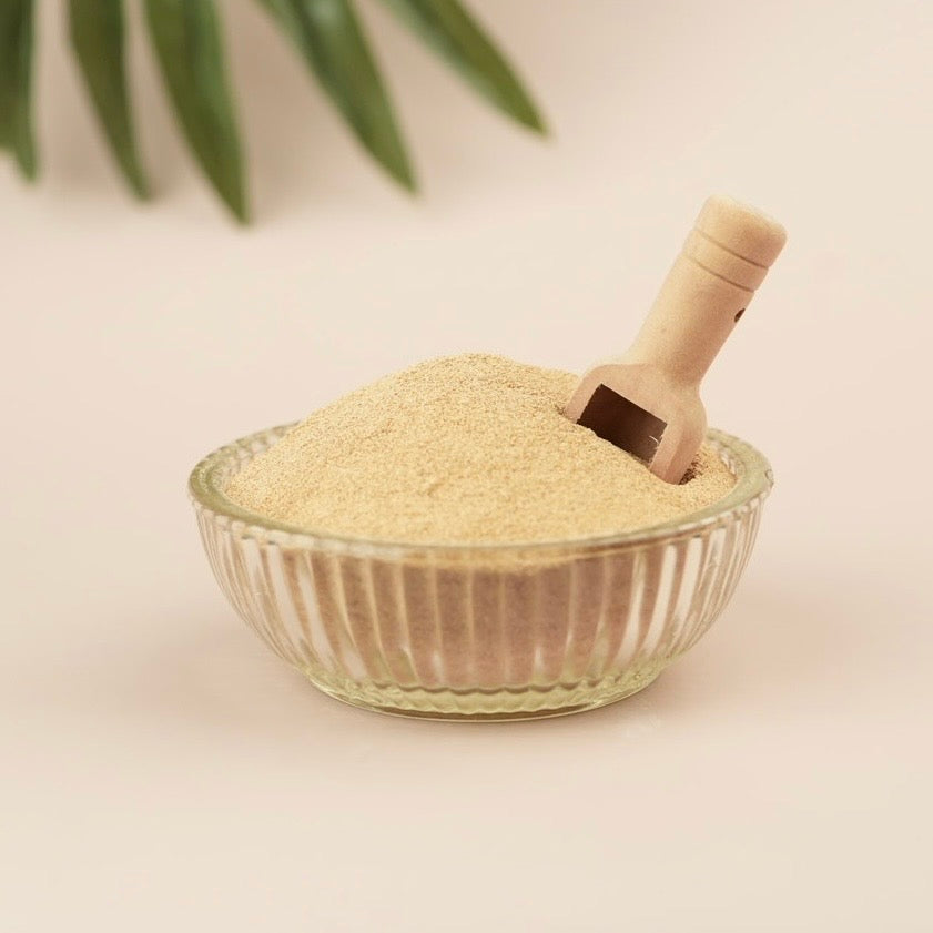 Glass bowl filled with light brown powder and a wooden scoop on a beige background