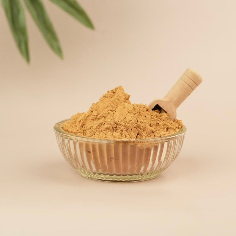 Glass bowl filled with brown powder and a wooden scoop on a beige background