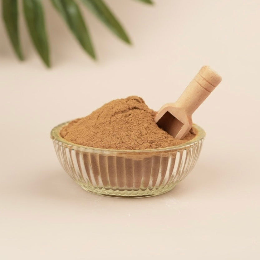 Glass bowl with brown powder and wooden scoop on a beige background