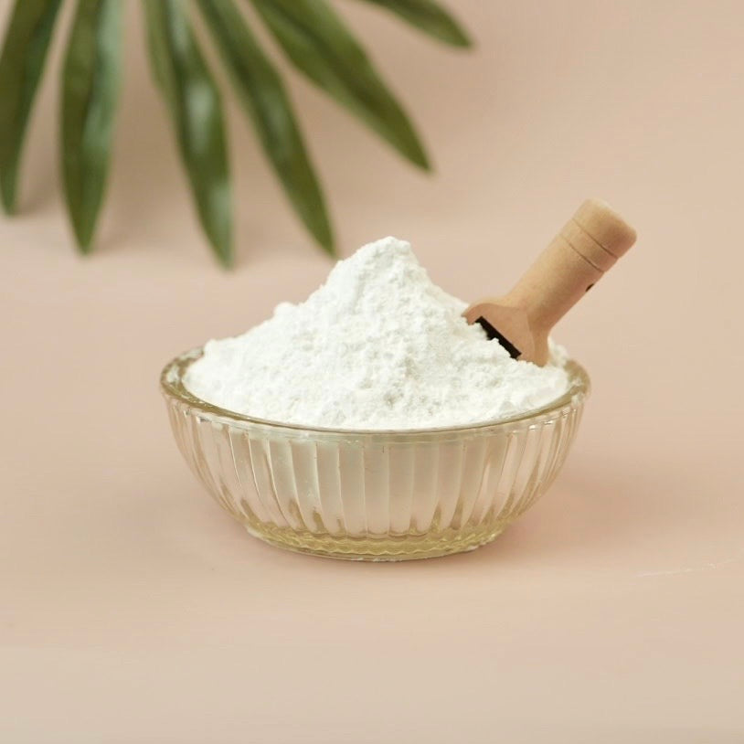 Glass bowl, white powder, wooden scoop and tan background