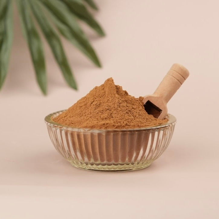Glass bowl filled with brown powder and a wooden scoop on a light background