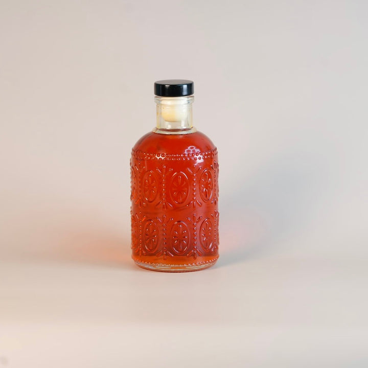 Bottle of amber liquid with a black cap on a light gray background