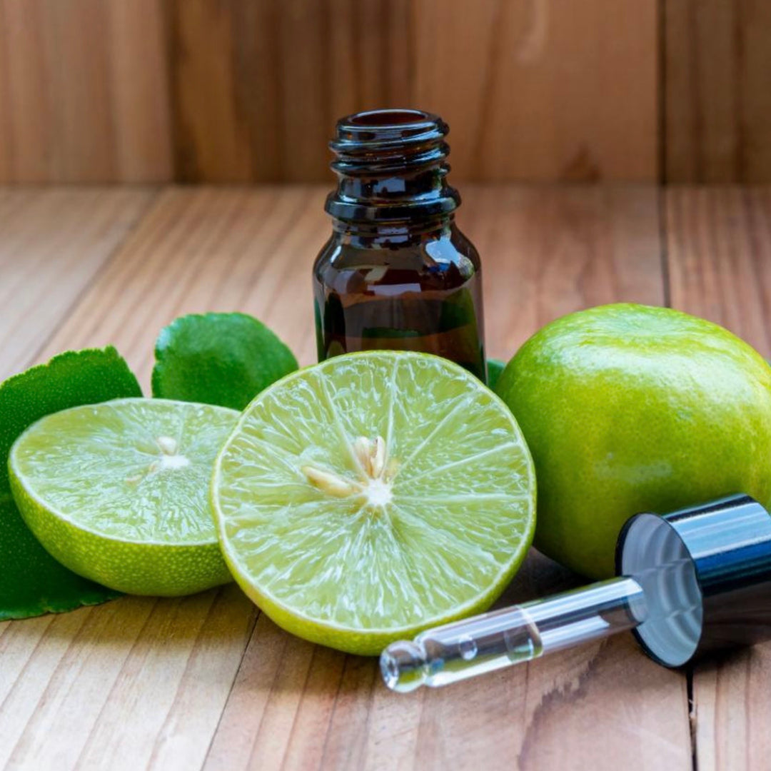 Bottle of essential oil with sliced limes on a wooden surface