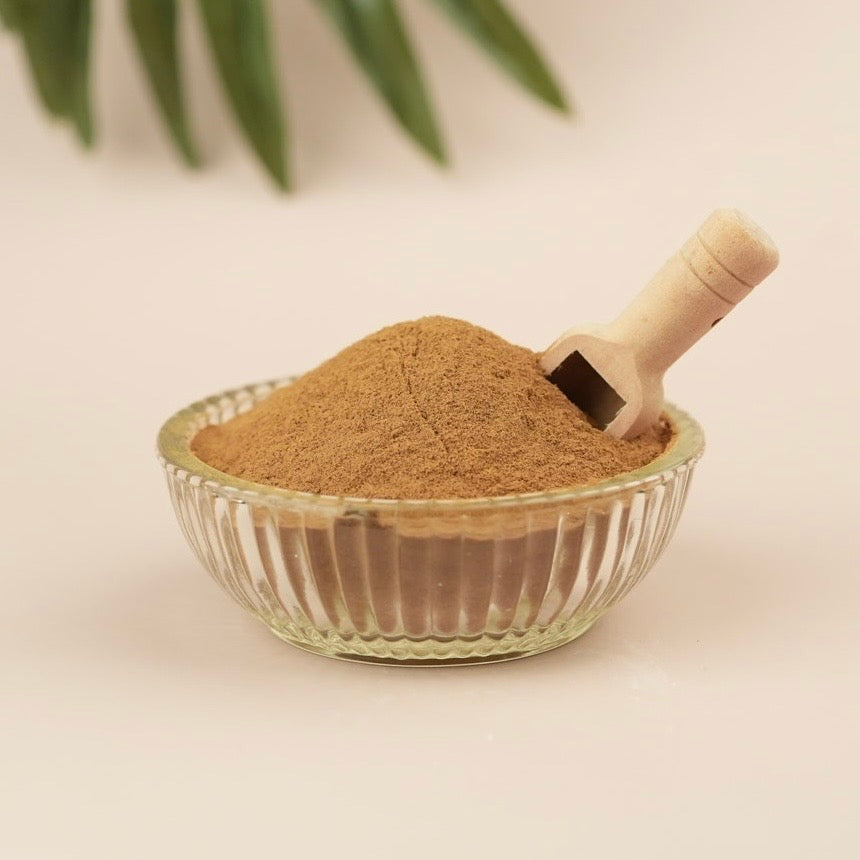 Glass bowl with brown powder and a wooden scoop on a light background