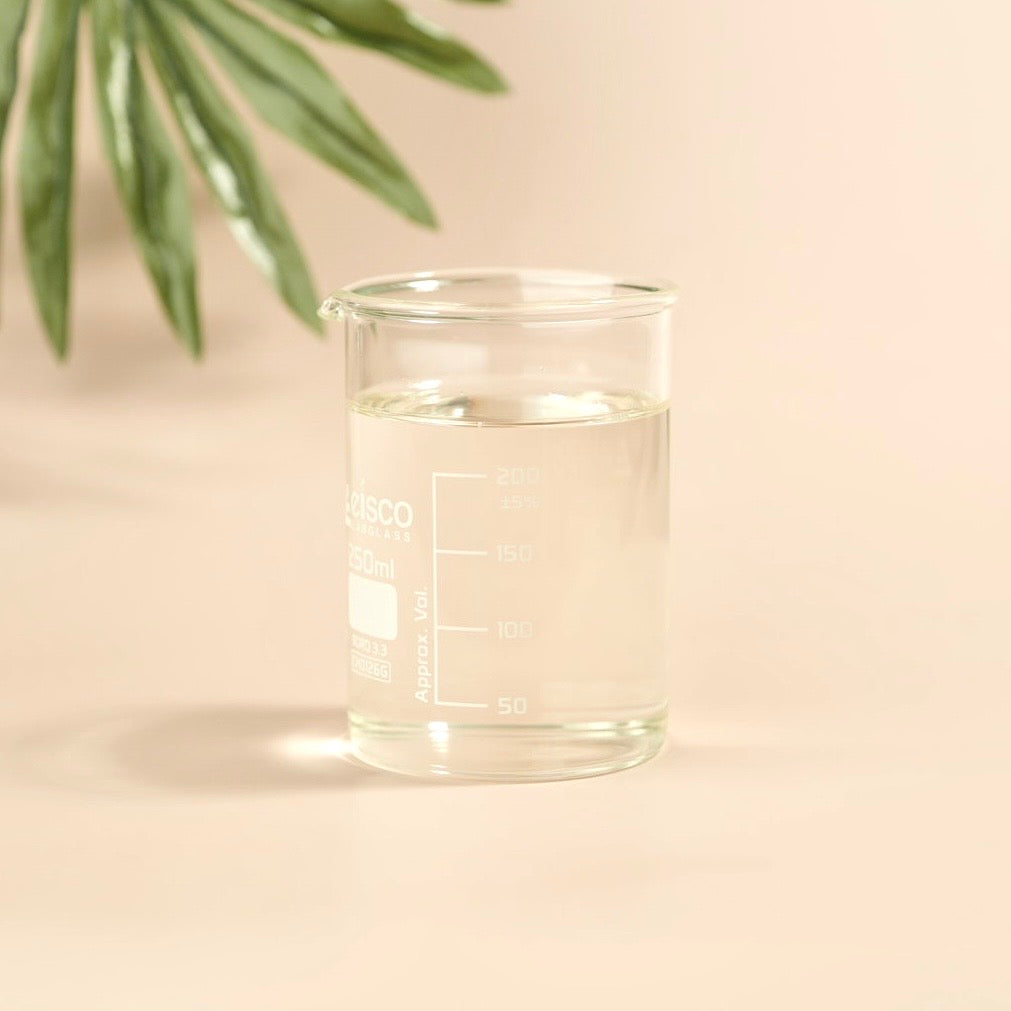 Clear glass beaker with liquid on a beige background with green leaves.