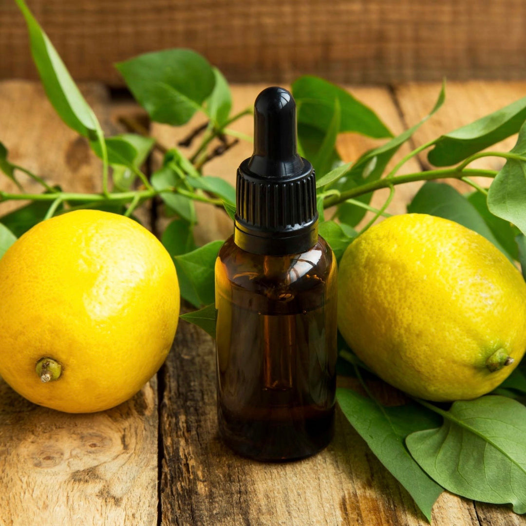 Brown glass bottle with dropper surrounded by lemons and green leaves on a wooden surface