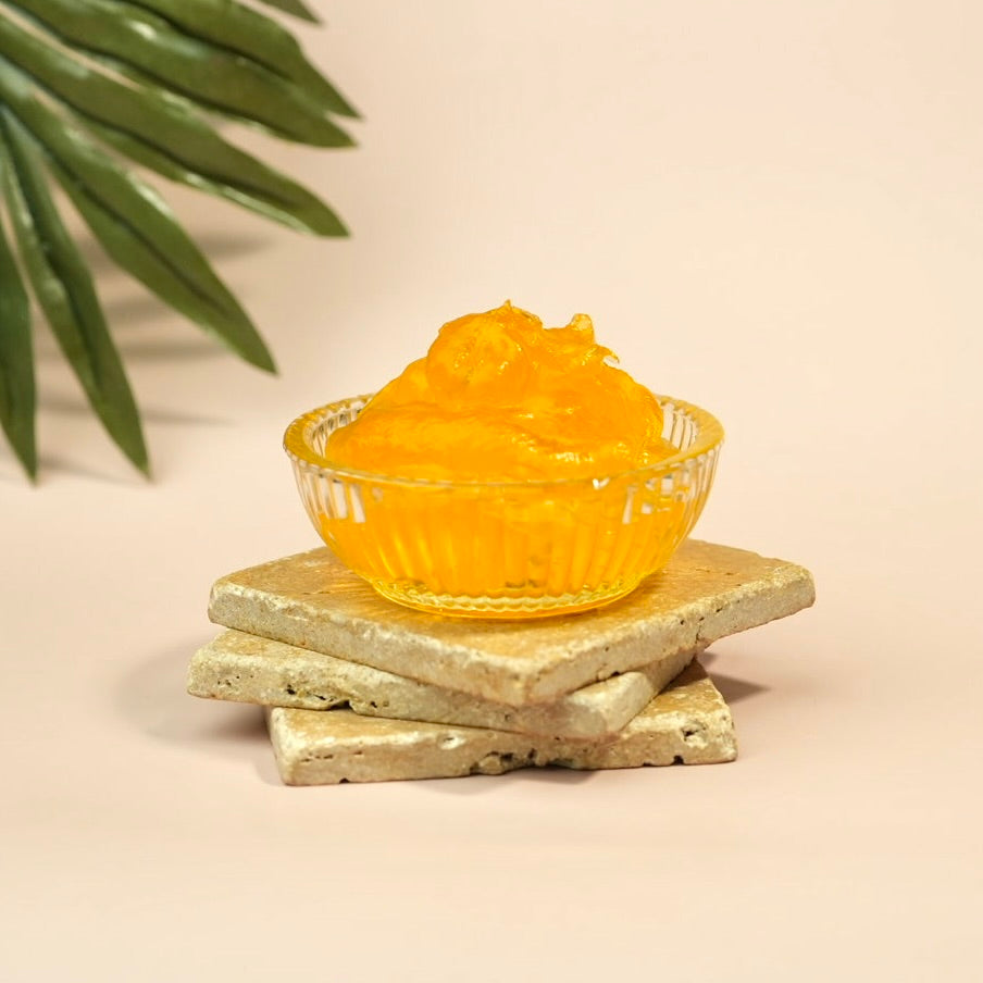 Clear glass bowl filled with yellow jelly on a beige surface with green leaves in the background