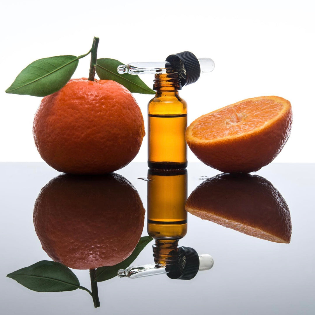 Amber glass bottle with black cap next to a whole and half orange on a reflective surface.