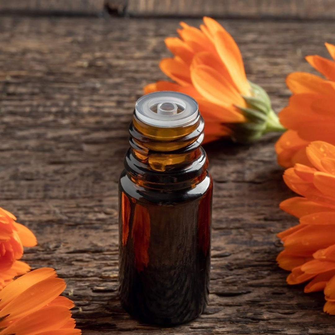 Brown glass essential oil bottle with a metal cap on a wooden surface with orange flowers.