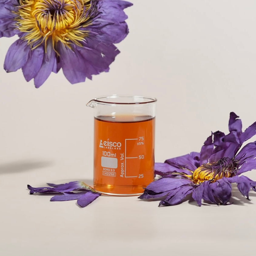 A 100ml clear glass beaker filled with amber-orange liquid, styled with purple flowers on a light beige background. The beaker is branded with 'letsco' and '100ml'.