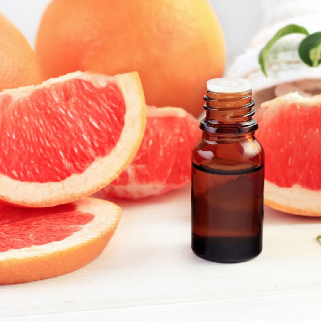 Bottle of essential oil with sliced grapefruits on a white background