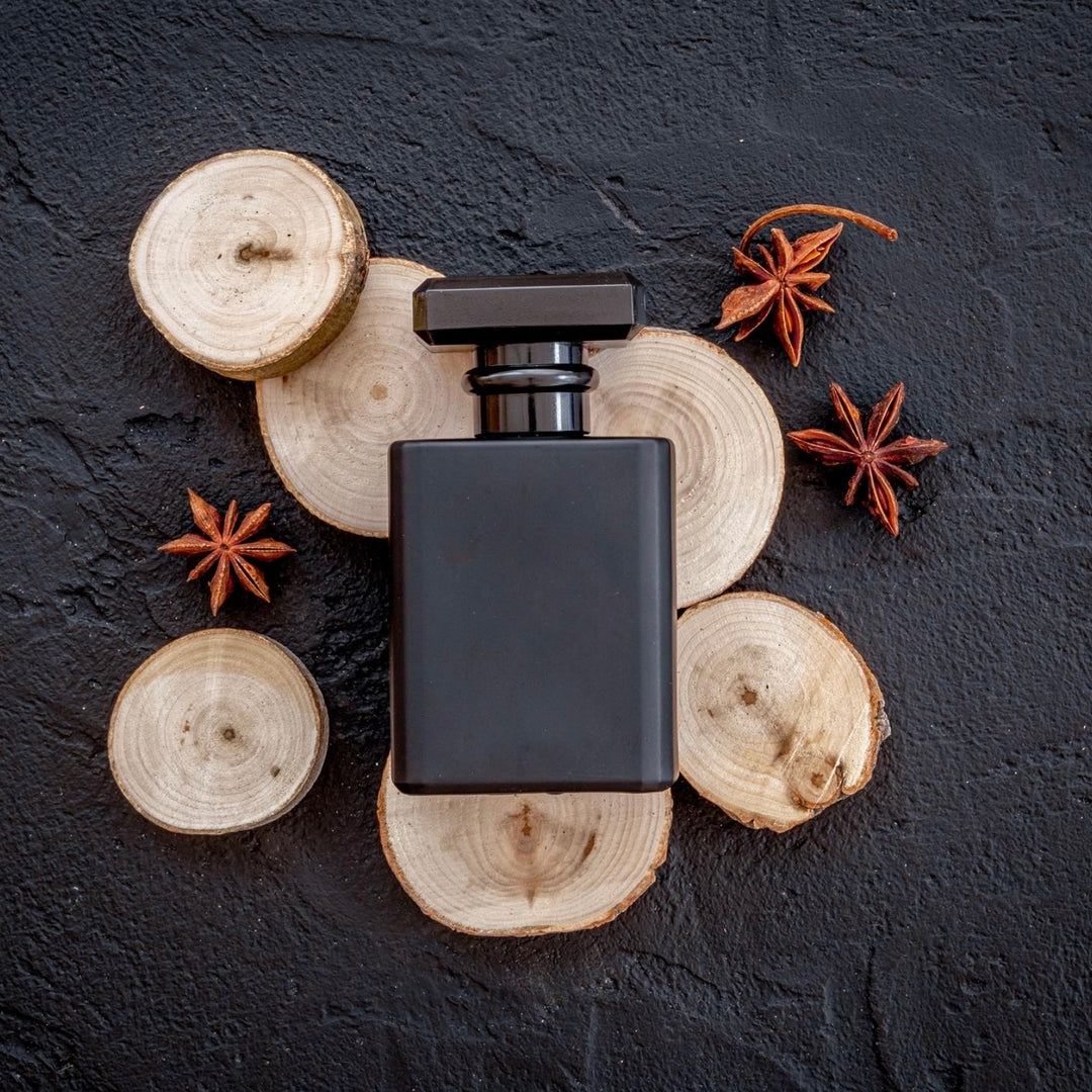 Black perfume bottle on wooden slices with star anise on a dark background