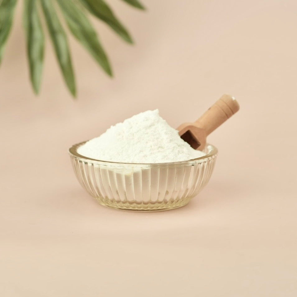 Glass bowl with white powder and wooden scoop on a beige background