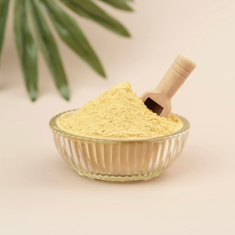 Yellow powder in glass dish with wooden scoop and beige background