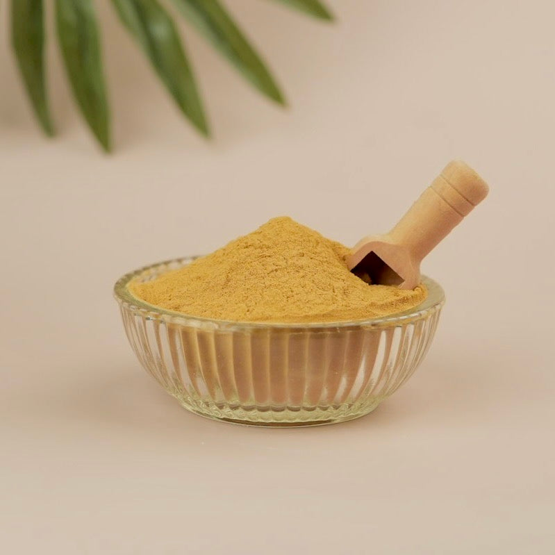 Glass bowl filled with yellow powder and a wooden scoop on a beige background