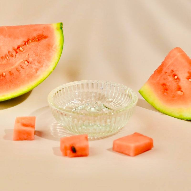 Sliced watermelon pieces and a clear glass bowl on a beige background