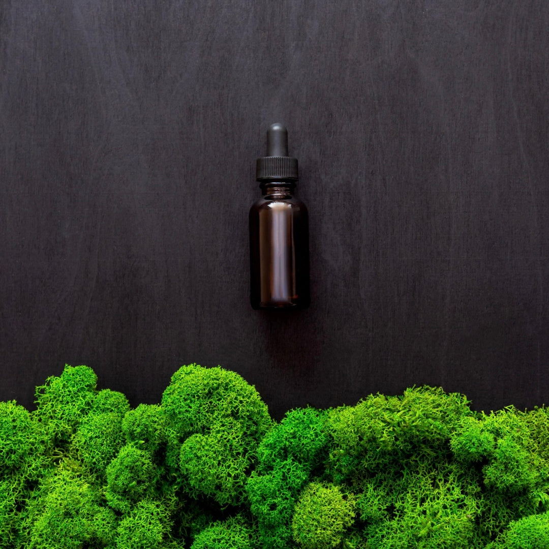 Brown glass dropper bottle on a black background with green moss at the bottom.