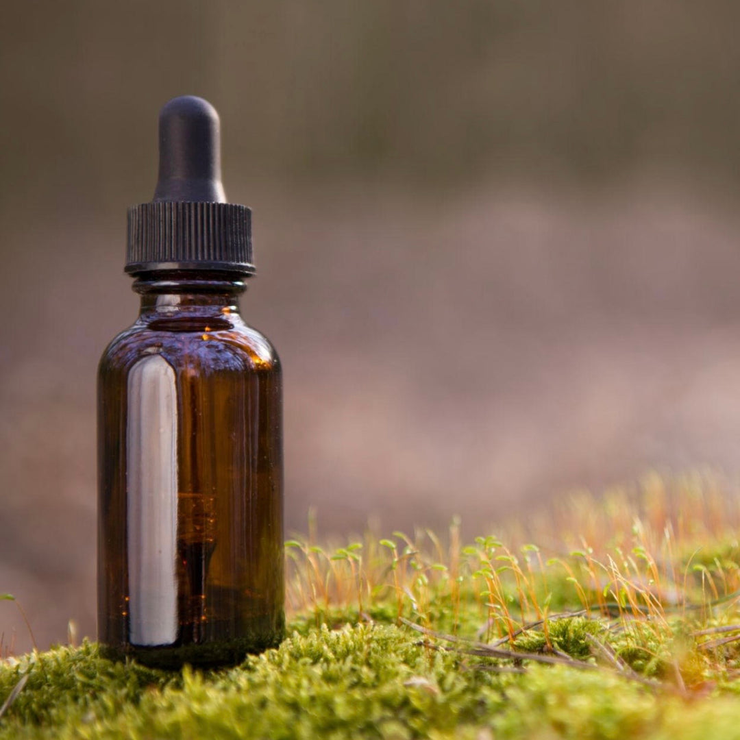 Brown glass dropper bottle on a grassy surface with a blurred natural background
