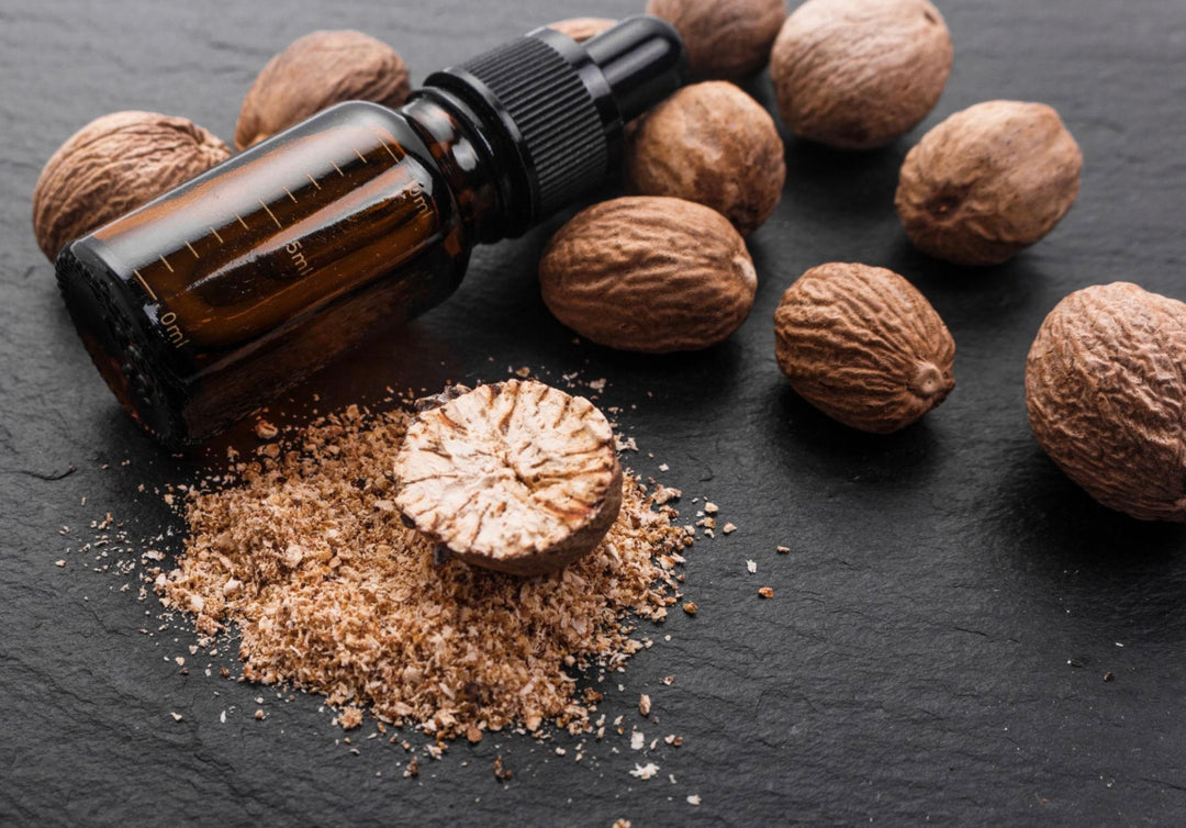 Brown essential oil bottle with nutmeg and ground nutmeg on a dark surface