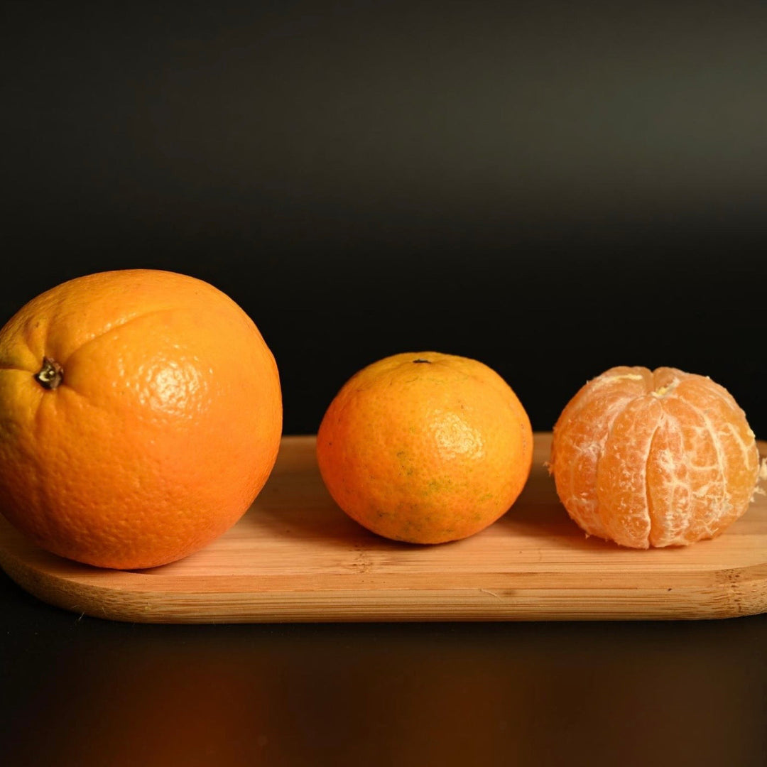 Three oranges on a wooden tray against a black background