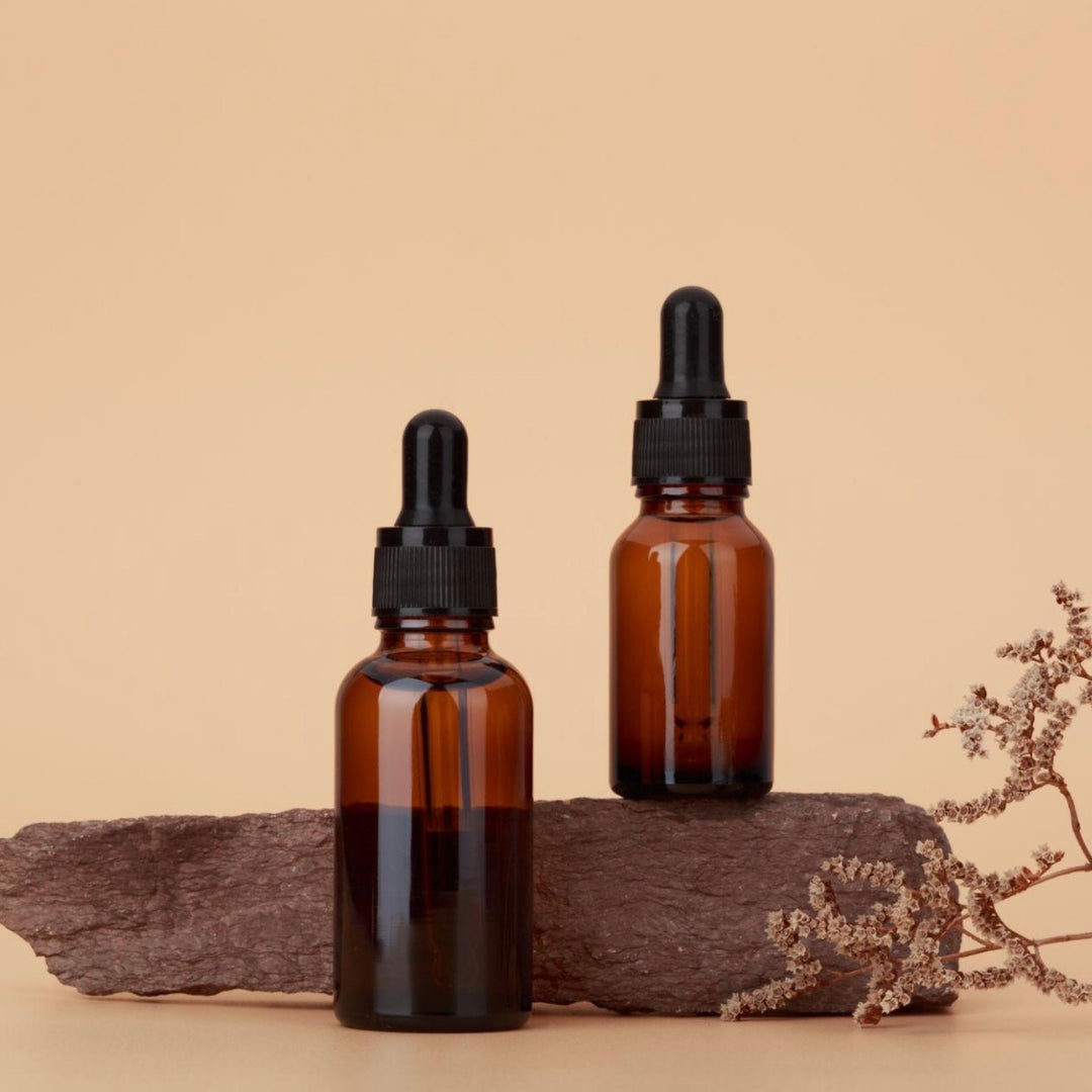 Two amber glass dropper bottles on a beige background with dried plants.