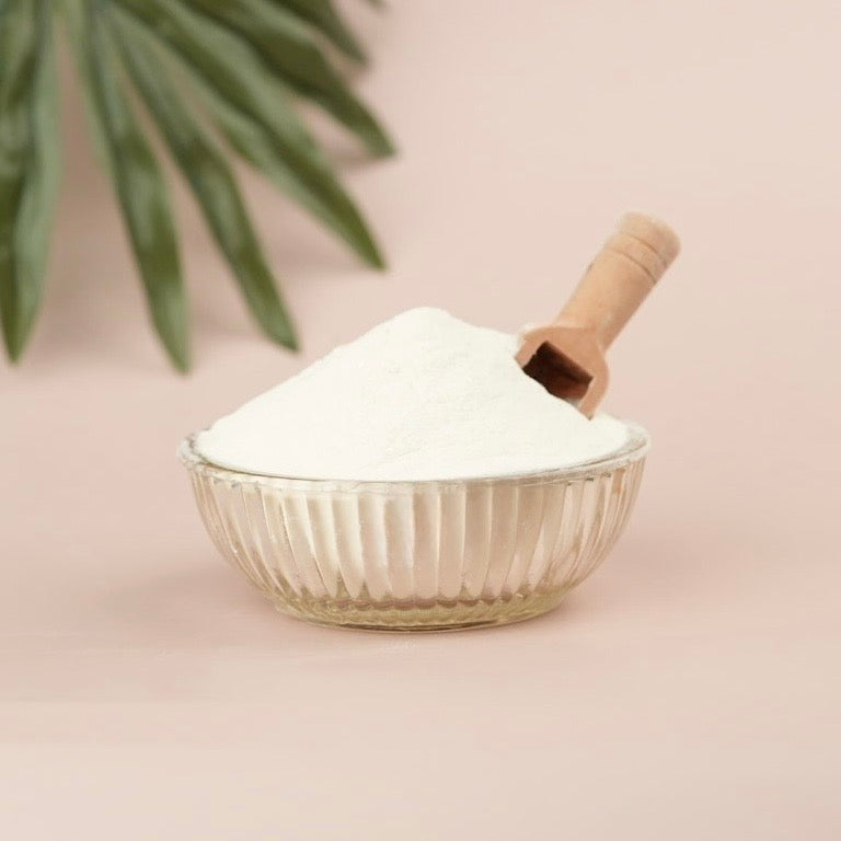 Glass bowl filled with white powder and a wooden scoop on a light pink background