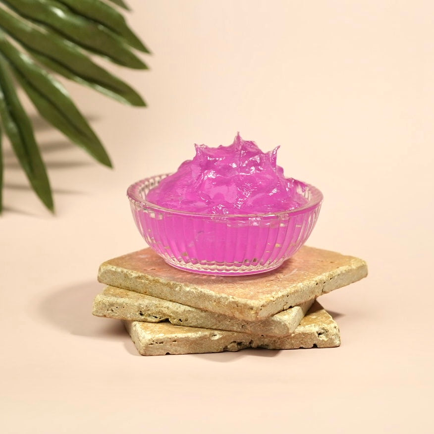Pink gel in a glass bowl on a beige surface with green leaves in the corner