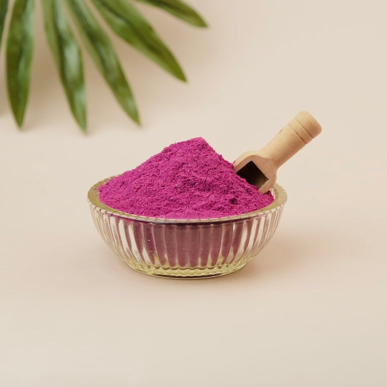 Purple powder in a glass bowl with a wooden scoop on a beige background