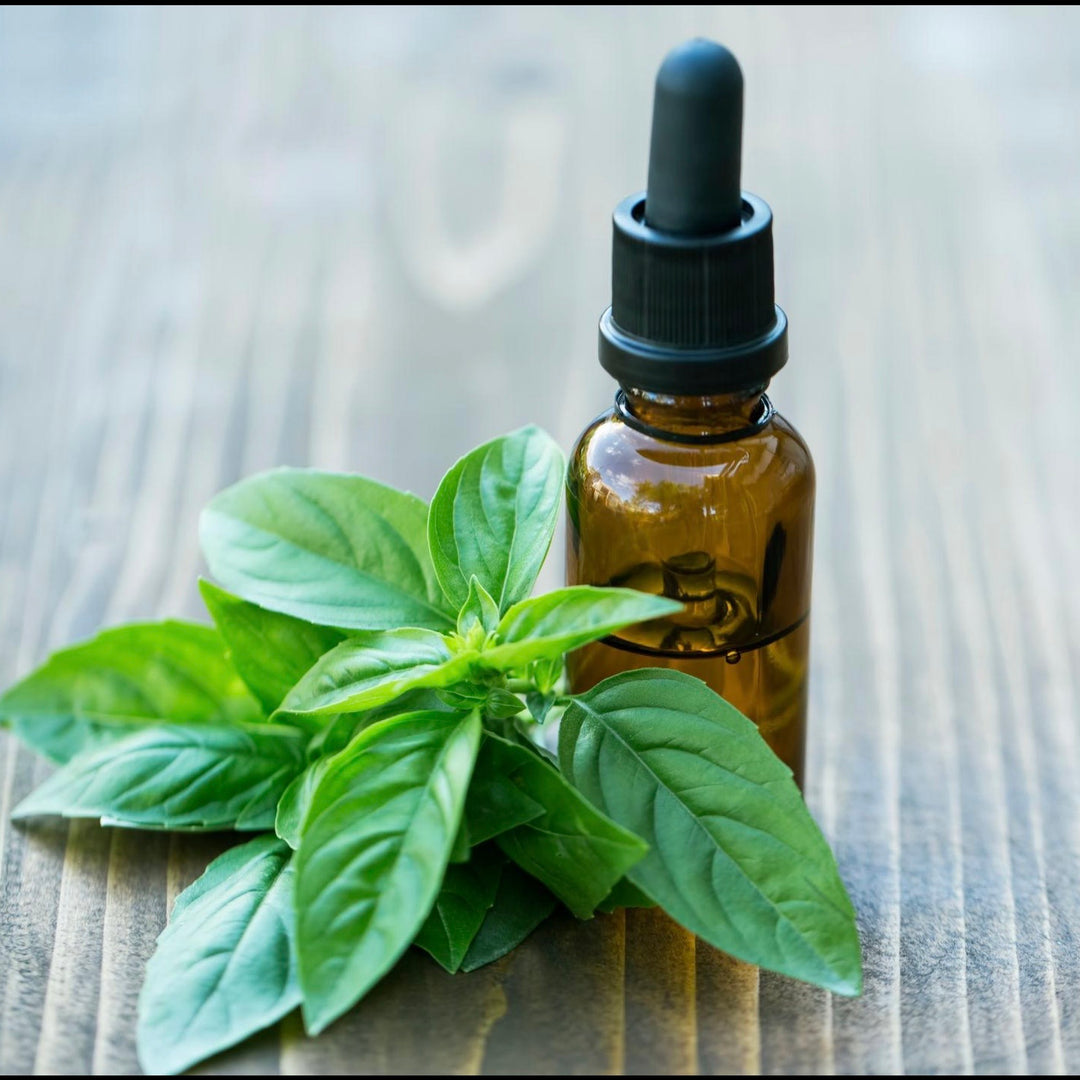 Brown glass dropper bottle with black cap next to fresh basil leaves on a wooden surface