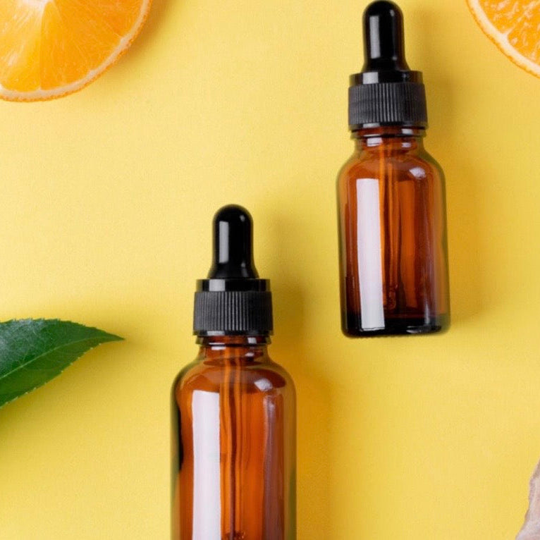 Two brown glass dropper bottles on a yellow background with orange slices and leaves.