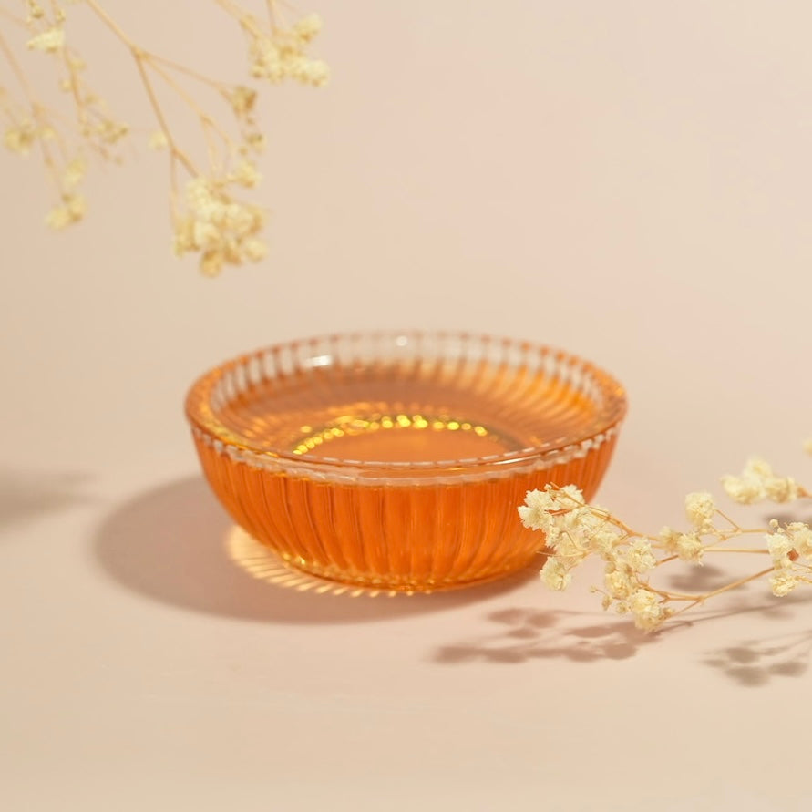 Clear glass bowl with honey on a beige background with dried flowers