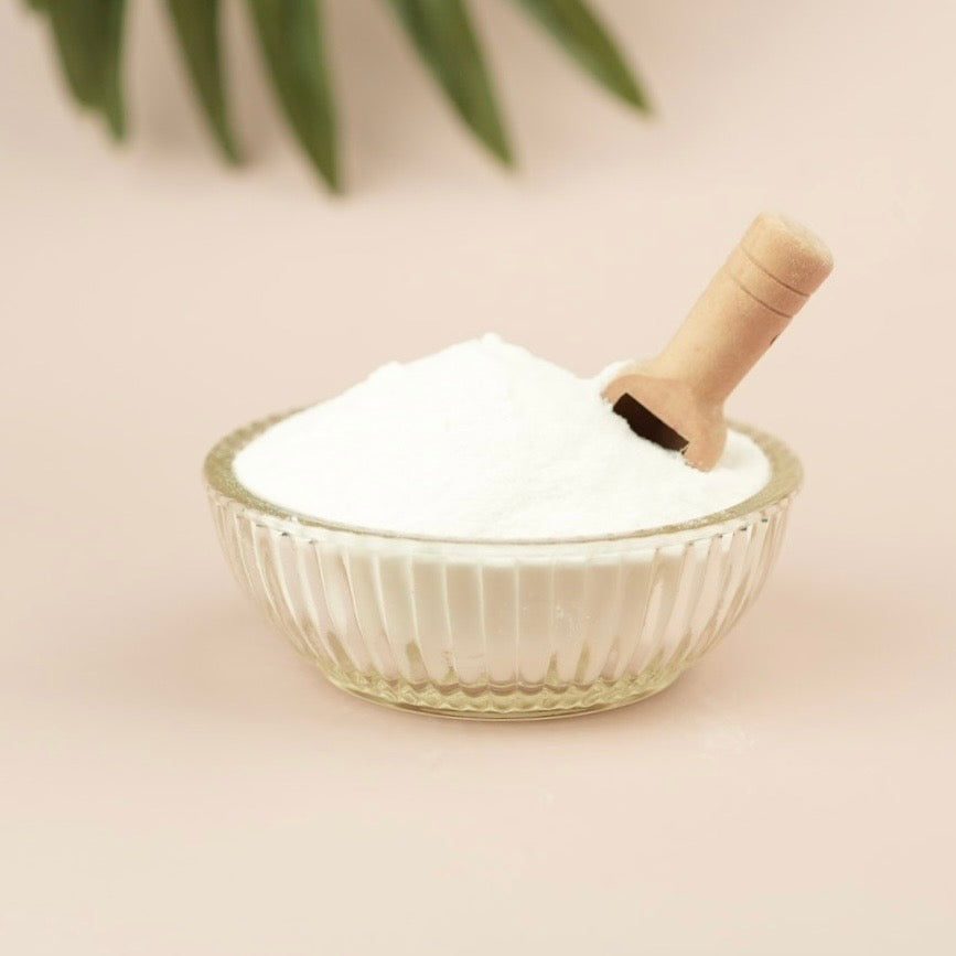 Glass bowl with white powder and a wooden scoop on a light background