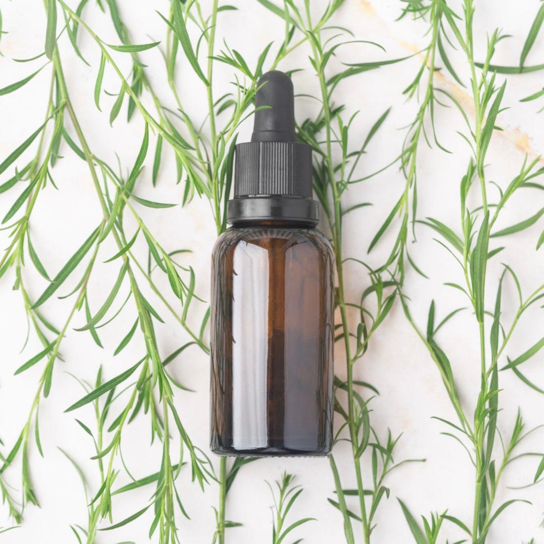 Brown glass dropper bottle with black cap on a white background with green leaves.