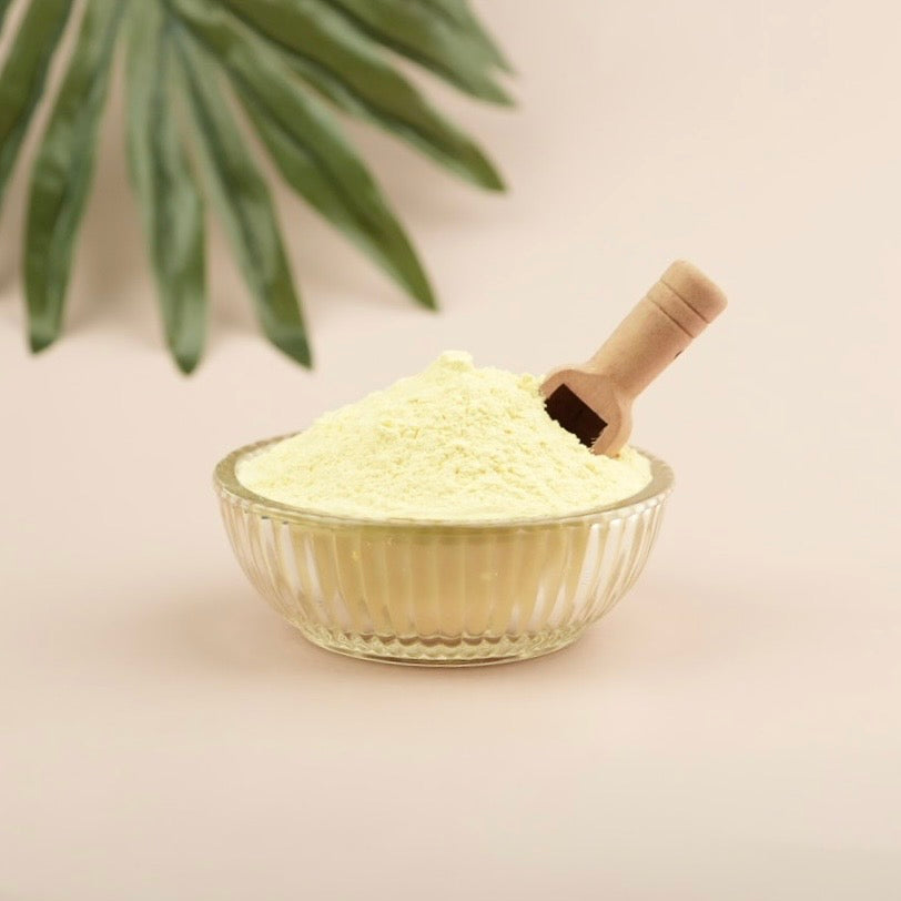 Glass bowl filled with light-colored powder on a neutral background with a wooden scoop.