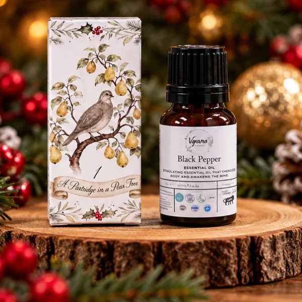 A bottle of Vynava Black Pepper essential oil next to its illustrated box, displayed on a rustic wood slice with a festive Christmas background.