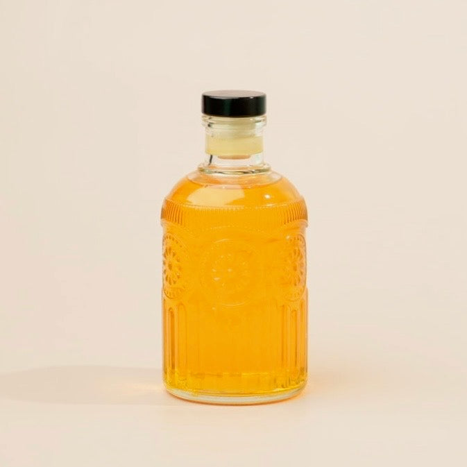Glass bottle with amber liquid and black cap on a beige background