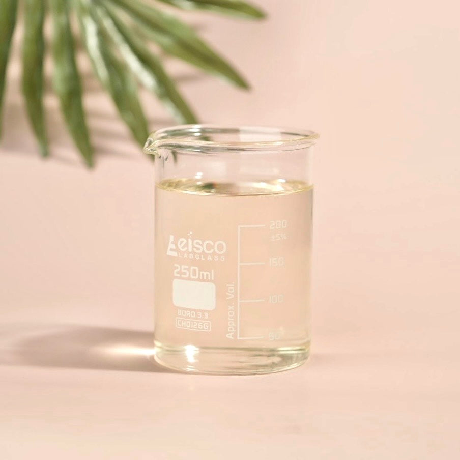 Clear glass beaker with liquid labeled 'Leisco' on a light pink background with green leaves.