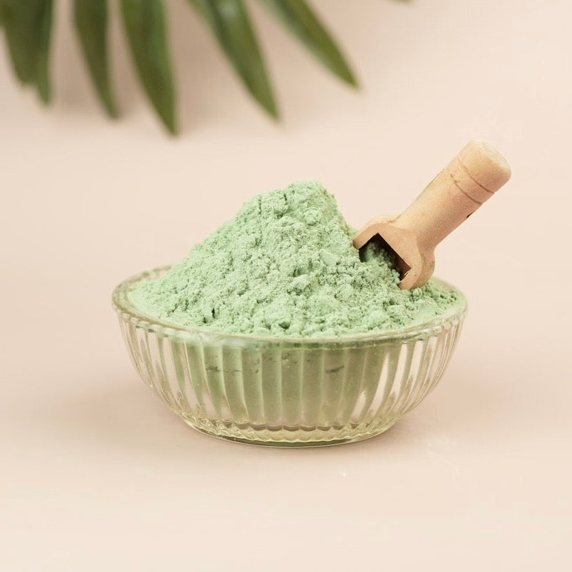 Glass bowl filled with green play sand and a wooden scoop on a light background